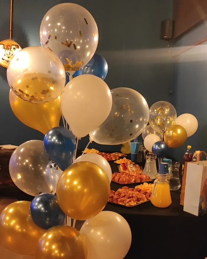 Globos dorados, blancos y azules junto a la mesa de comida de un cumpleaños en la sala