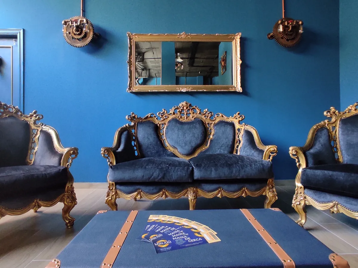 El salón de espera de la sala: sofás barrocos azules y dorados, un baúl y un espejo