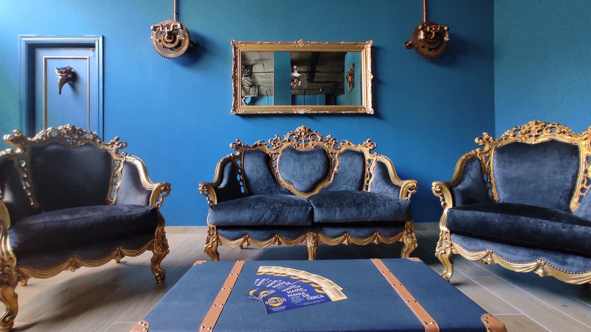 Salón de espera de la sala Mirari: tres sofás barrocos dorados, un baúl, un espejo y dos lámparas